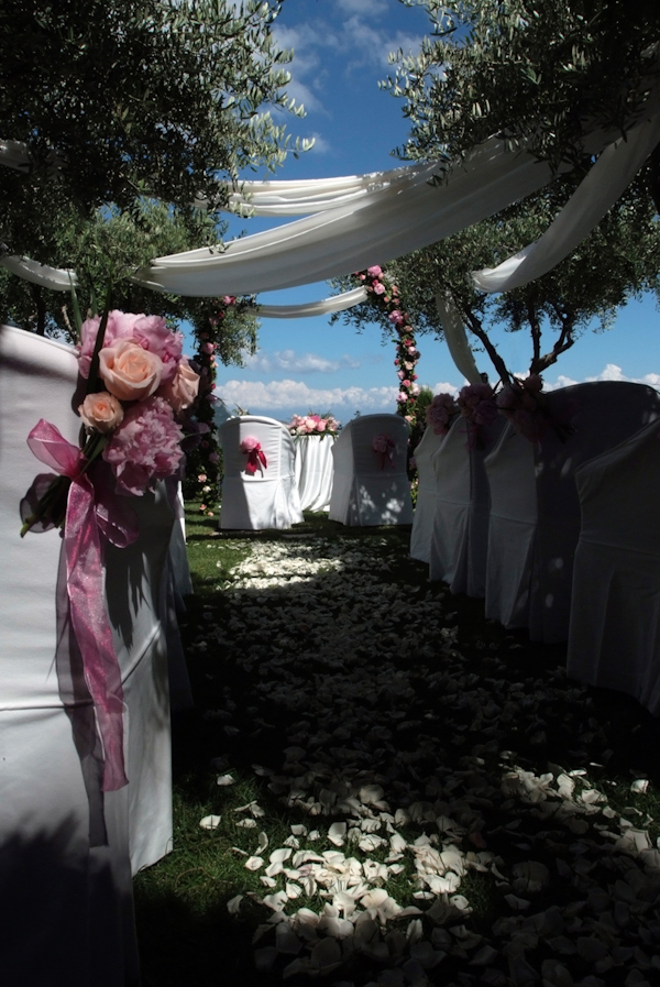 beautiful outdoor ceremony aisle decor - white silk draped from trees over the aisle covered with white rose petals and white seat covers with pink and peach floral decor - photo by Italian wedding photographer JoAnne Dunn